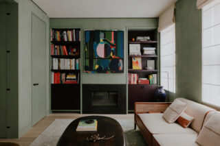 Interior townhouse living room shot. Dark wood bookcases, a painting, a couch, and coffee table in view.