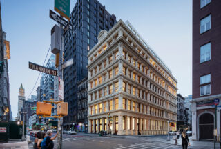 Street view shot of the Cast Iron House, emanating warm light from its windows.