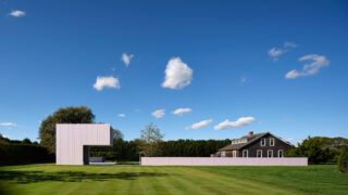 Exterior faraway shot of the Pink Pool House in the midst of a green landscape and blue sky.