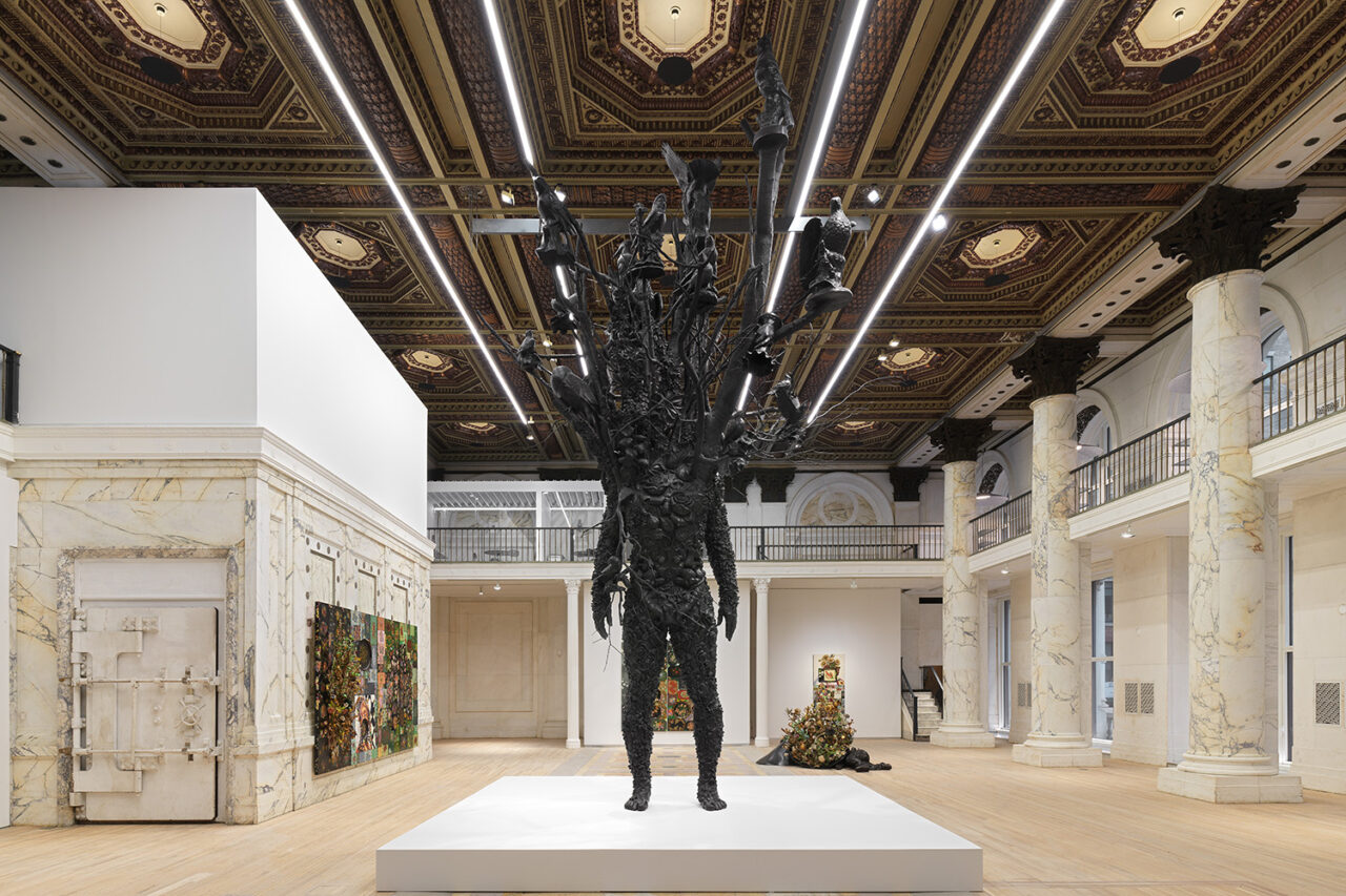 Interior shot of art gallery with a Nick Cave sculpture of a figure on the central white podium.