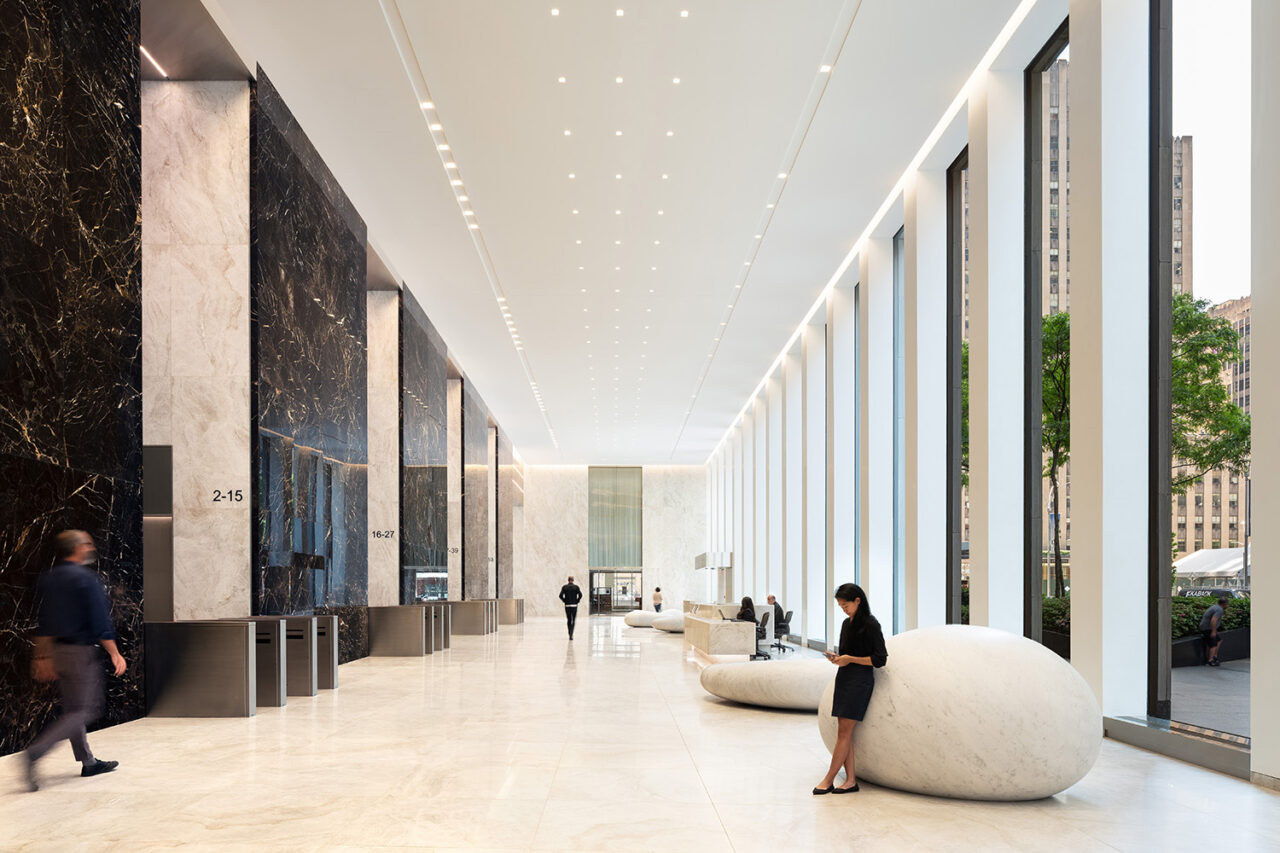 Interior entryway/hallway shot with white flooring and ceilings. Elevators on the left, large windows to the right.