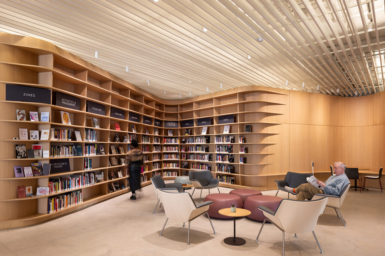 Photo of reading room with floor to ceiling bookshelves. A man in a chair reading and a woman browsing the shelves.