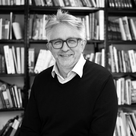 Black and white headshot of Nico Kienzl in front of a bookshelf filled with books