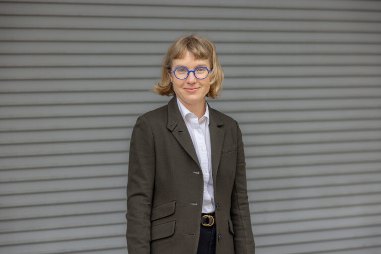 Headshot of a white woman with short blonde hair wearing a gray blazer.