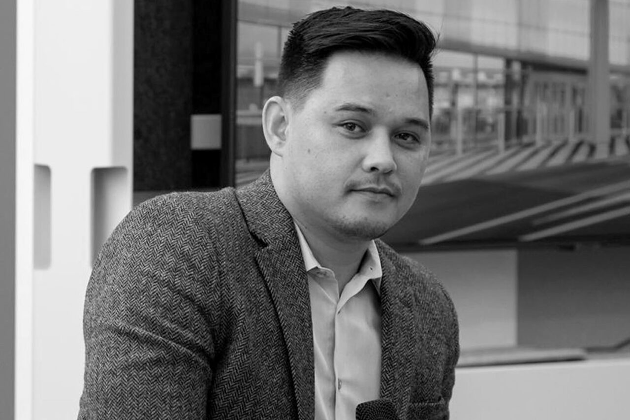 Black and white headshot of a light-skinned man with short black hair wearing a button up and suit jacket.
