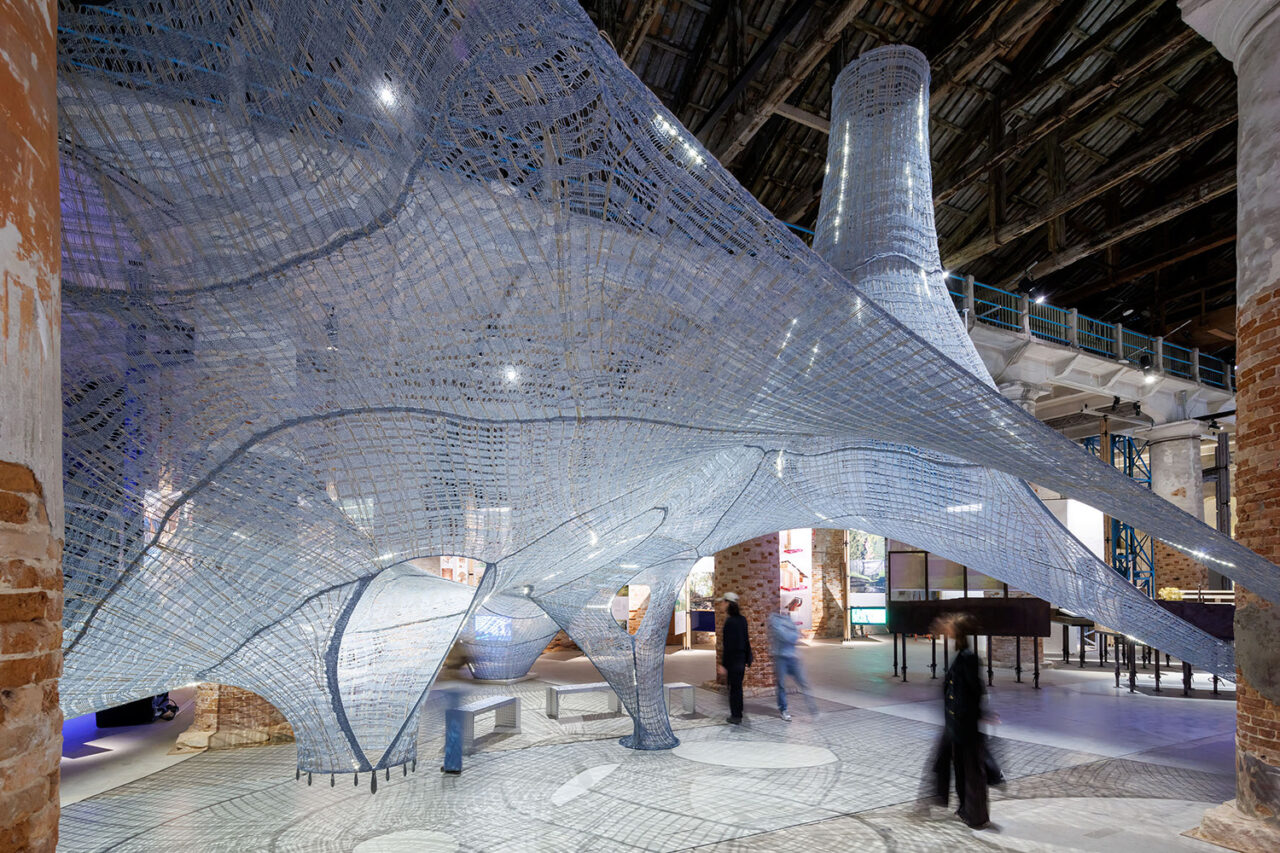 Passersby walk through a suspended knitted installation.