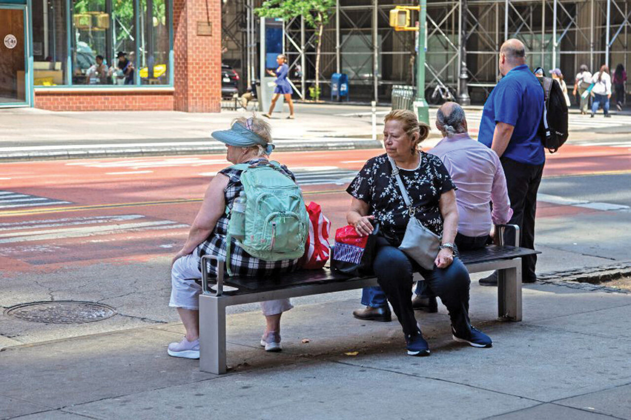 Several people seated on a bench on a sidewalk