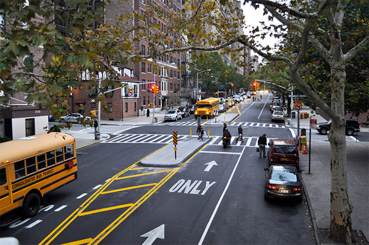 A city street with parked cars and school buses on either side