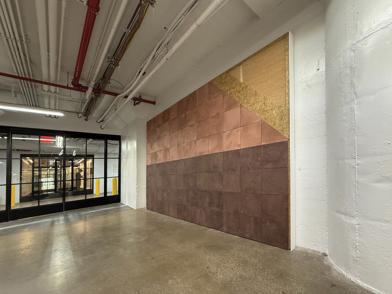 An empty room with a concrete floor and a feature wall of textured tiles in various shades of brown