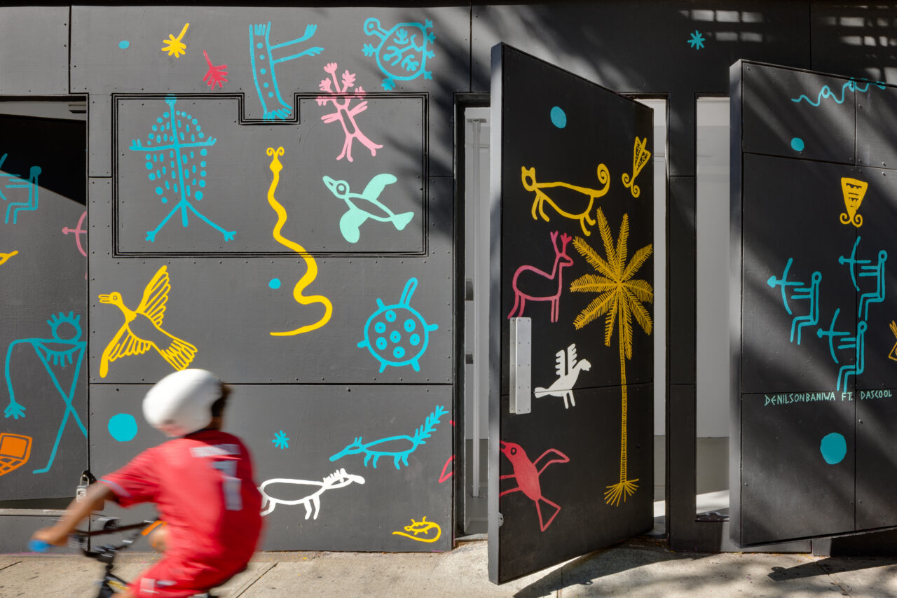 A colorful mural of naturalistic animals and humans on a black exterior facade of the the Storefront for Art and Architecture