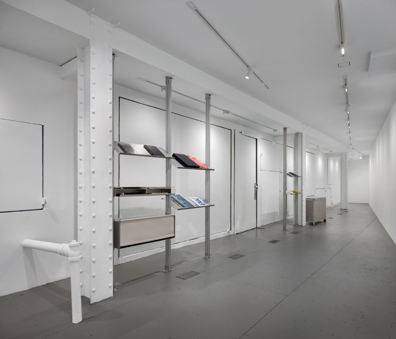 Interior of the Storefront for Art and Architecture renovation by GRT Architects: a long, mostly empty stark white room with metal shelving holding reading material