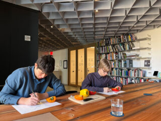 Two student seated at a table drawing cut up peppers