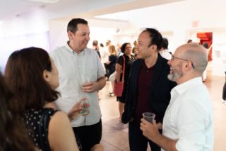 Photo of a group of individuals in semi-casual attire standing in a circle and talking jovially