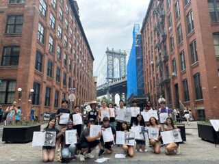 High school students posing with their sketchbooks in front of the Manhattan Bridge.