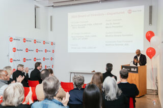 A man speaking at a podium and a room of people seated and listening