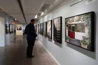Man standing in front of a series of framed photographs in a long hallway